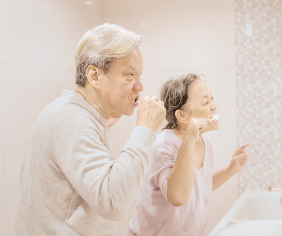 Duas pessoas idosas escovando os dentes. Parece que uma imita a outra ou ensina